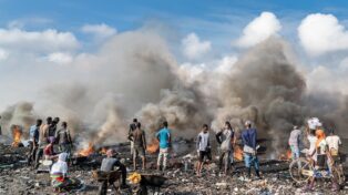 Décharge de déchets électronique. Des hommes et femmes noires près d'un feu de déchet, avec un grand nuage de fumée.