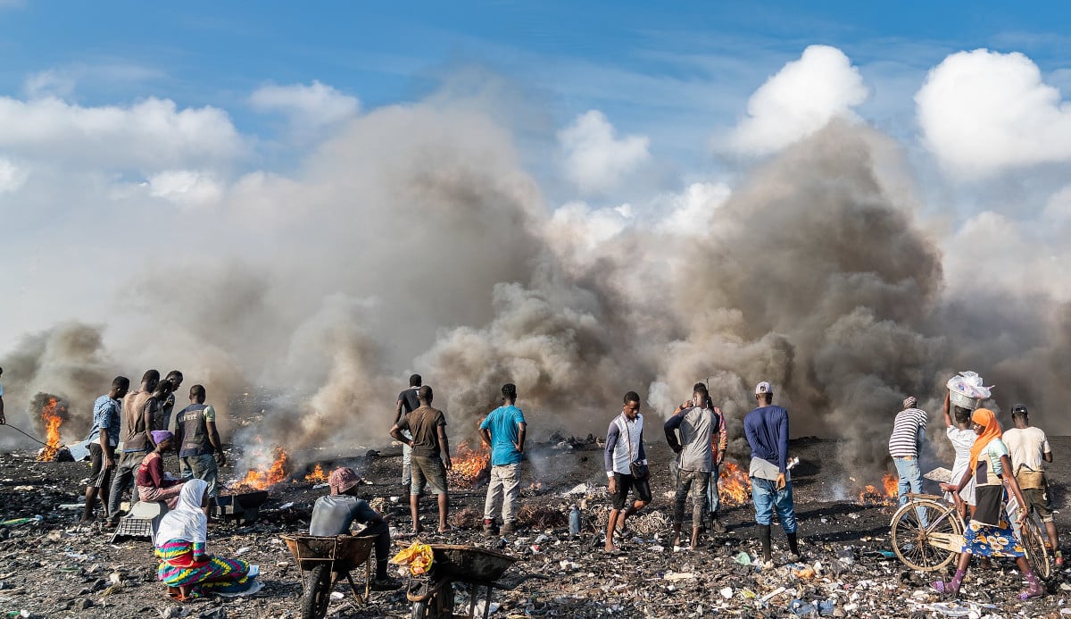 Décharge de déchets électronique. Des hommes et femmes noires près d'un feu de déchet, avec un grand nuage de fumée.