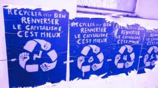 Quatre affiches dans la rue : "Recycler c'est bien, renverser le capitalisme c'est mieux". Chaque affiche contient une lettre : N O U S.