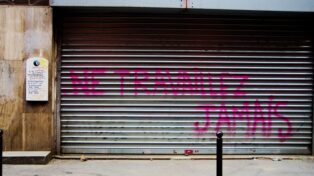 Un rideau métallique fermé, tagué "Ne travaillez jamais". C'est un Pôle emploi.