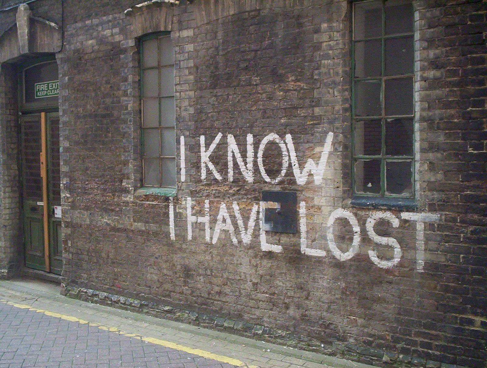 "I Know I Have Lost" (Je sais que j'ai perdu) écrit en grand sur un mur de briques sombes.