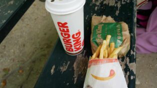 Une boisson burger king, un burger végétairen encore emballé, des frites. Le tout sur un banc dans un parc.