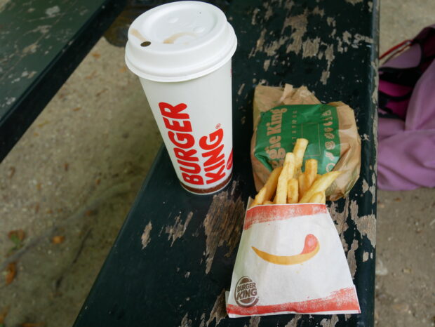 Burger, boisson et frites sur un banc public dans un parc.