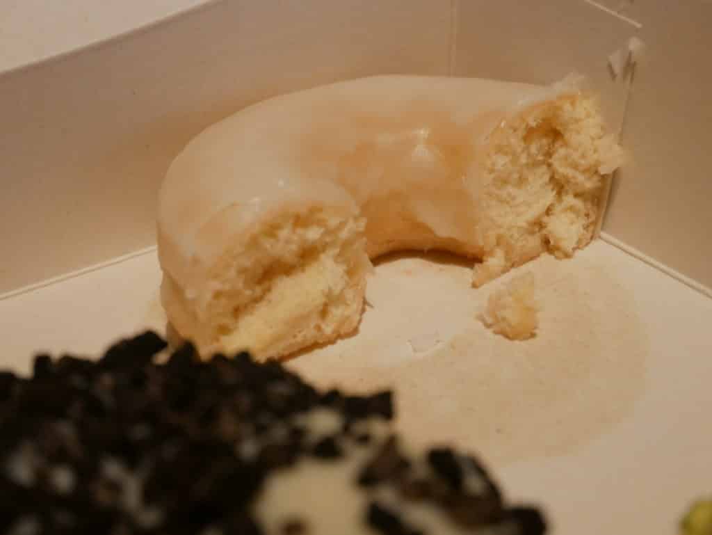 Un donut glacé à moitié coupé, au fond d'une boite, avec des traces de gras et une mauvaise luminosité.