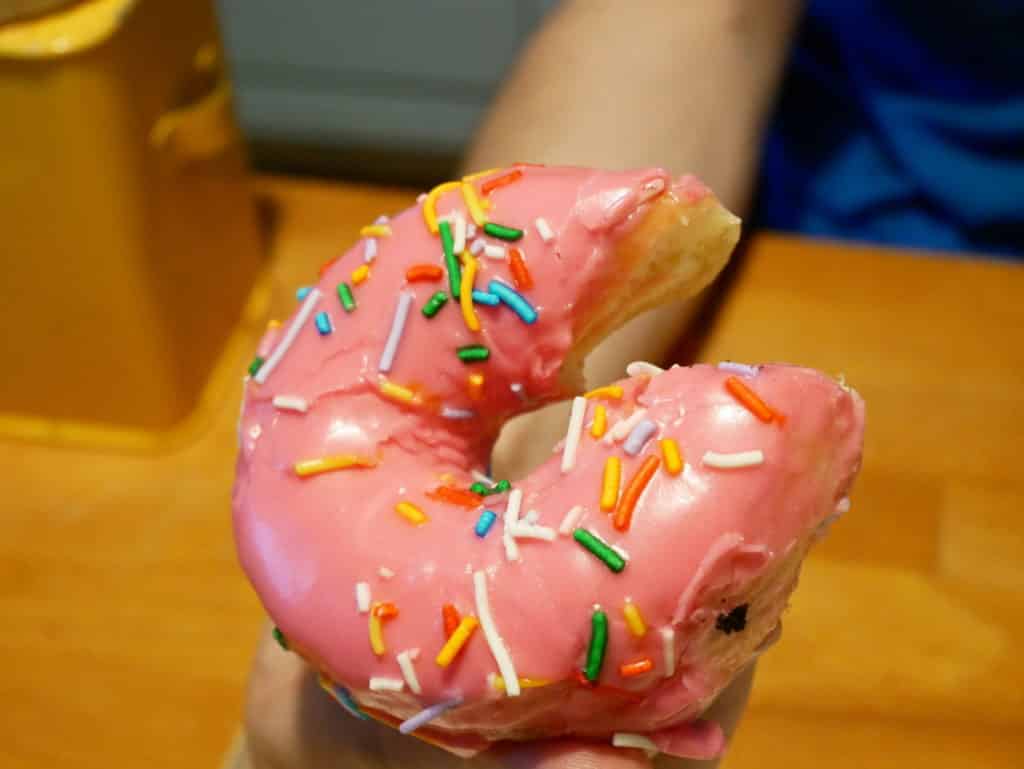 Un donut rose "Simpson" tenu dans une main, bien éclairé et avec le point.