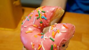 Un donut rose "Simpson" tenu dans une main, bien éclairé et avec le point.