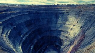 Énorme mine creusée dans le sol. La fosse prend toute l'image. En haut, on voit en tout petit la ligne d'horizon d'une grande ville.