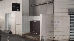Urinoir collé à un mur. Un panneau indique l'urinoir. À côté, un renfoncement dans lequel on a taggué "Interdit d'uriner ici".